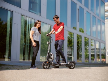 People standing with an e-scooter in front of a university building. 