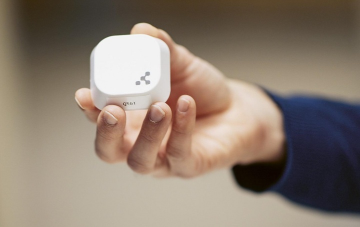 One hand holds a white cube-shaped sensor into the camera