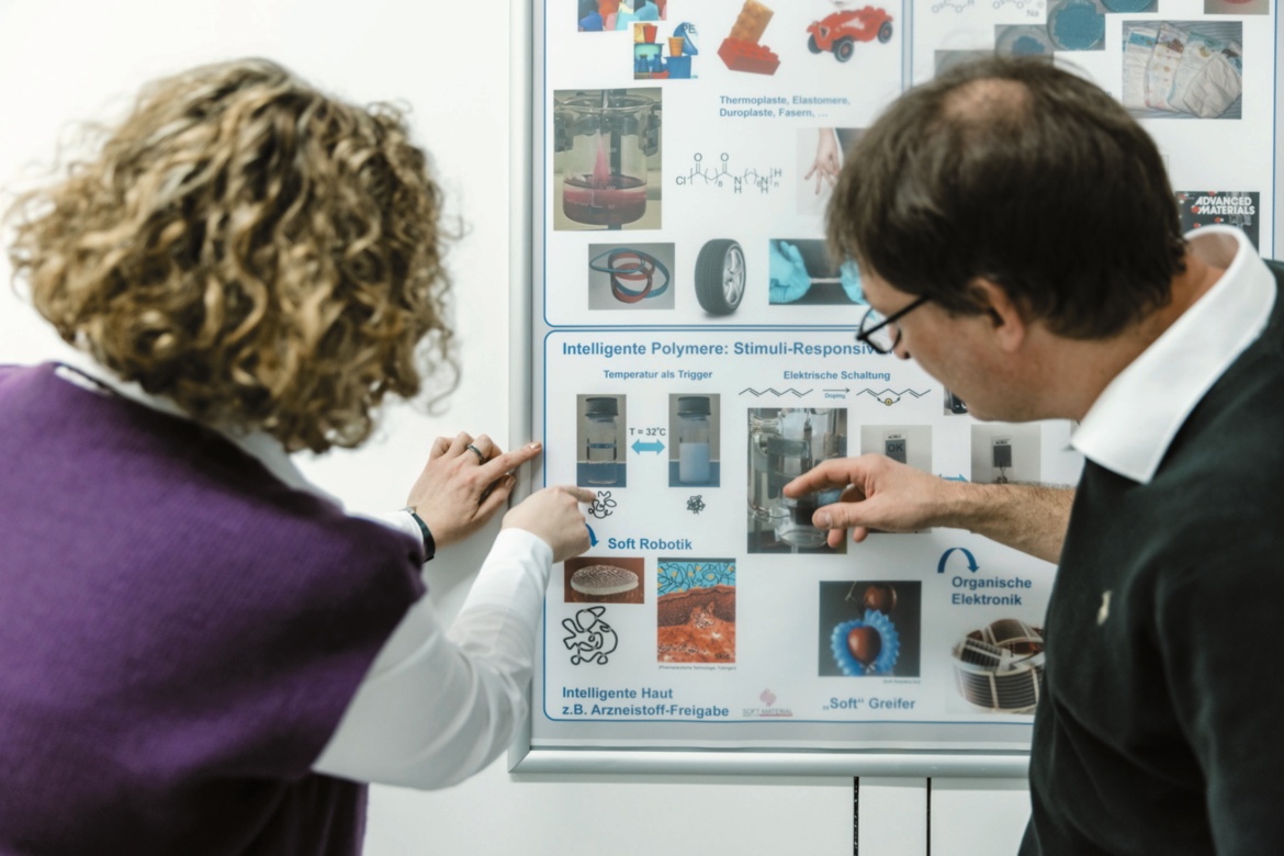 Prof. Sabine Ludwigs und Prof. Holger Steeb betrachten die Möglichkeit zur Nutzung von Polymeren für die Medizin auf einem Poster