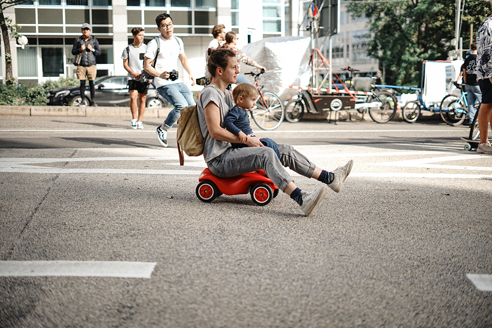Erwachsener mit Kind auf dem Schoß rollt auf dem Bobycar über die Straße