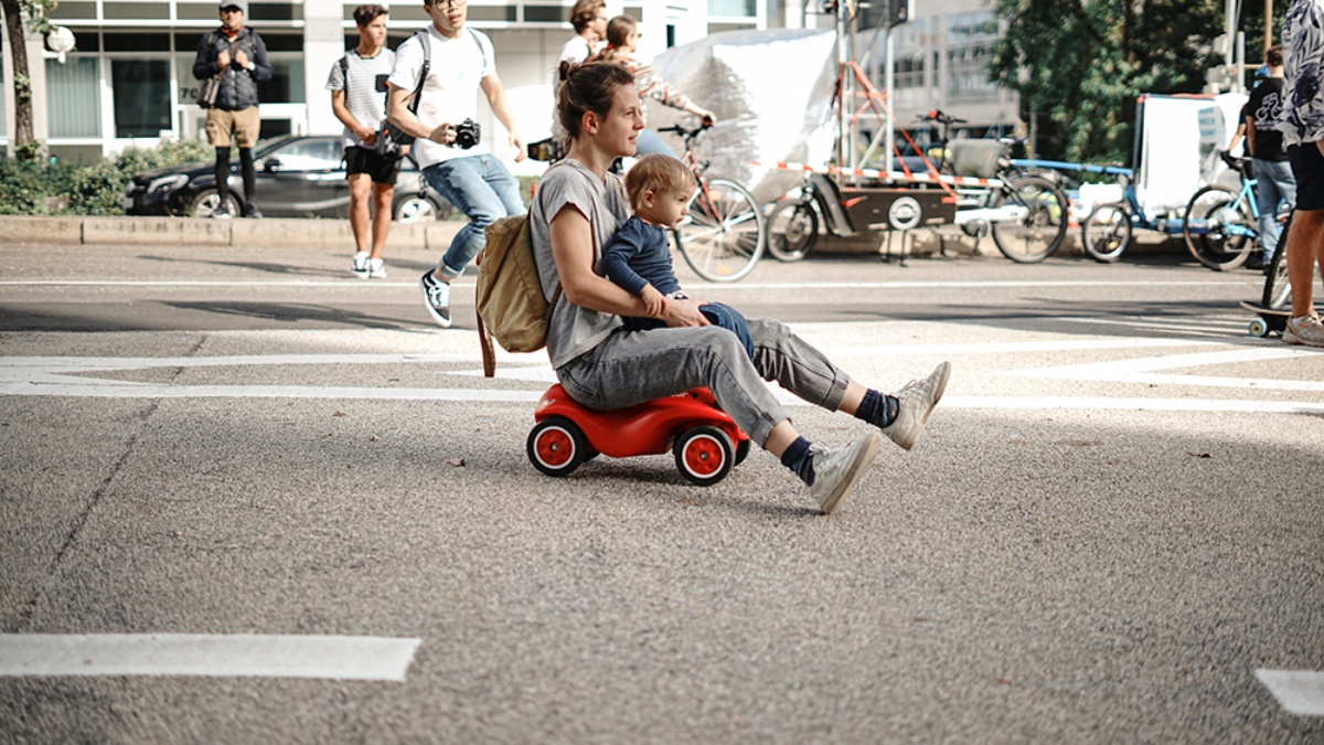 Erwachsener mit Kind auf dem Schoß rollt auf dem Bobycar über die Straße