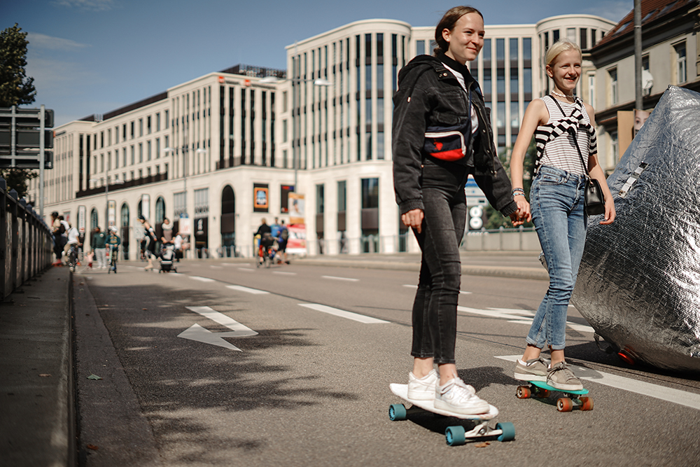 Zwei weibliche Teenager fahren Hand in Hand mit dem Skateboard über die Straße