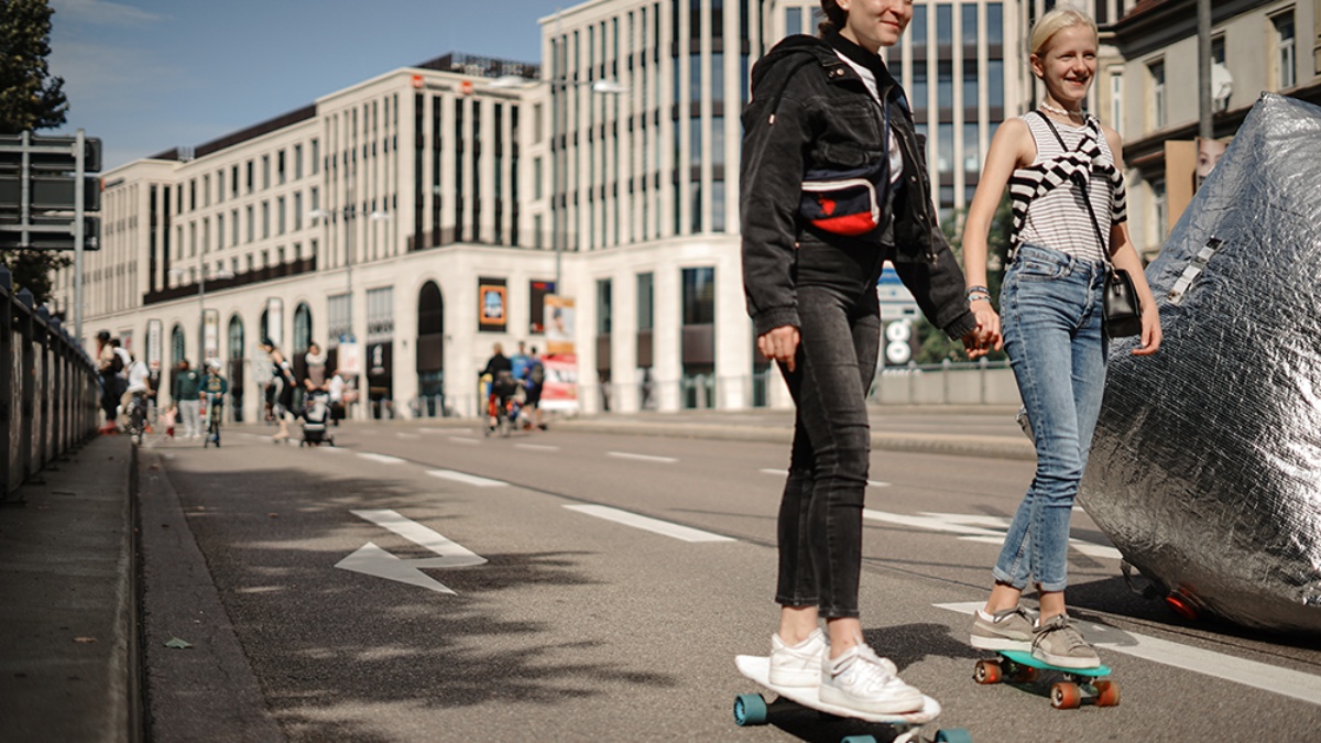 Zwei weibliche Teenager fahren Hand in Hand mit dem Skateboard über die Straße