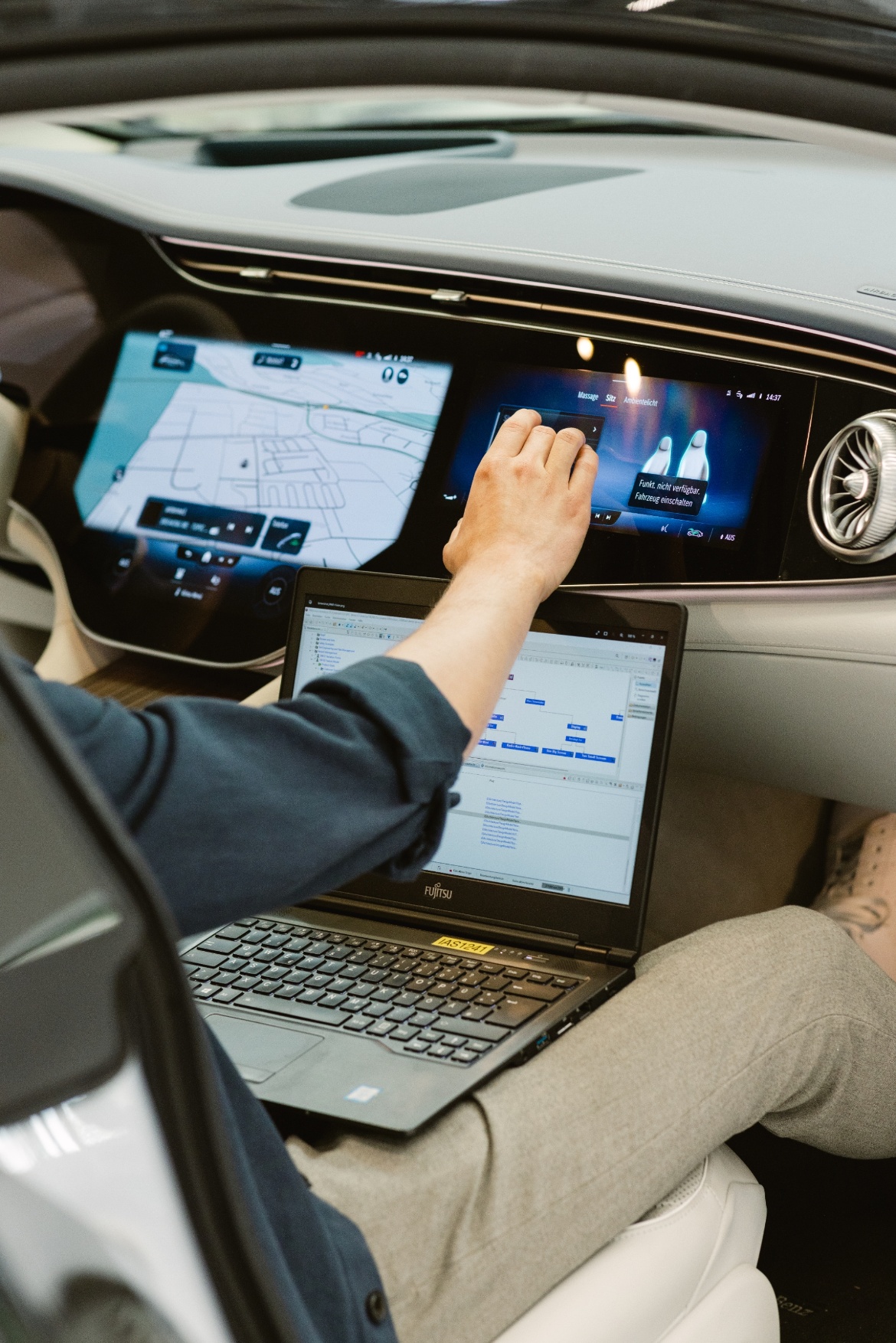 A person with a laptop on its knees sits in a car. 