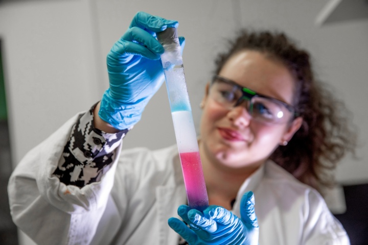 Eine Frau in einem Labor hält ein Reagenzglas mit Flüssigkeit darin.