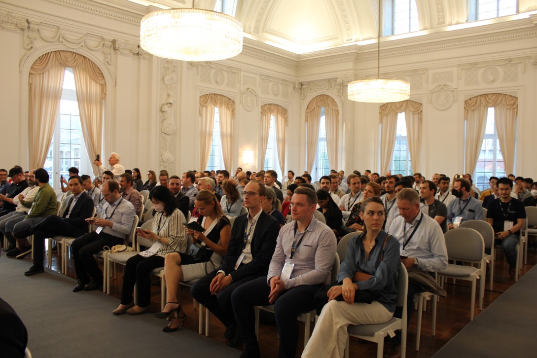 Viele Konferenzbesucher sitzen in mehreren Reihen in einem großen Festsaal.