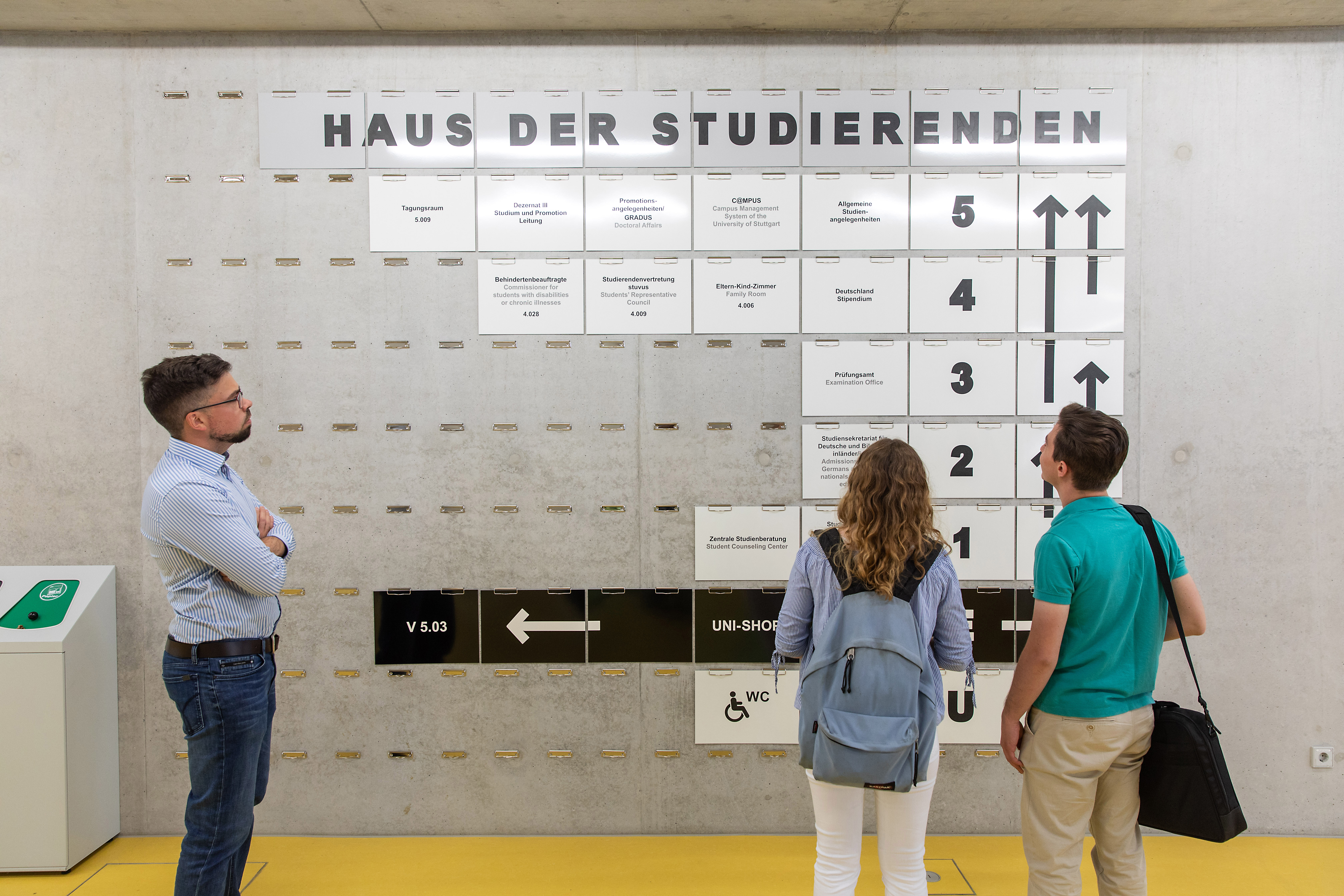 Students looking on the signboard of the house of students of the University of Stuttgart.