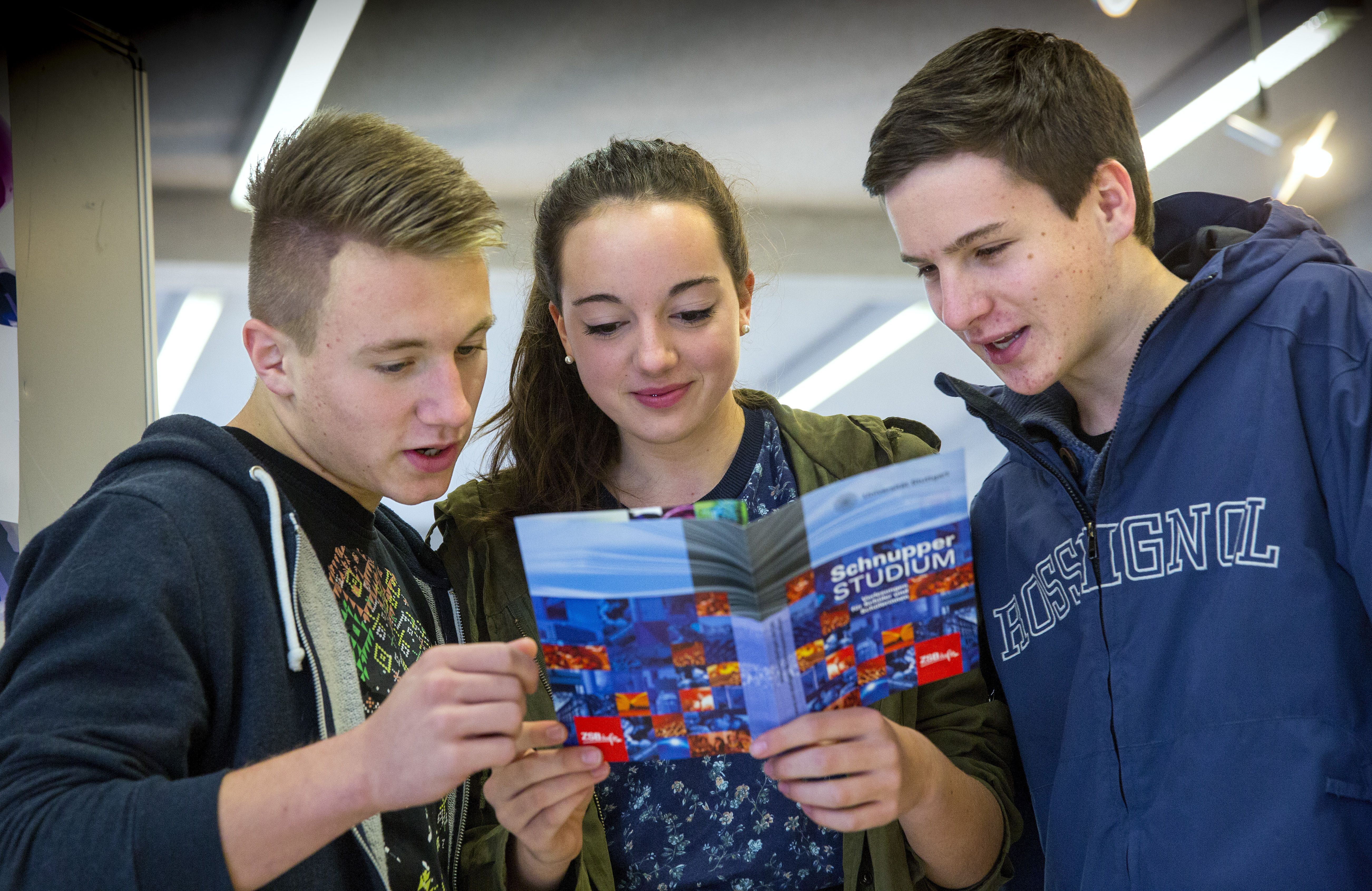 Schülerinnen und Schüler lesen gemeinsam einen Flyer über ein Schnupperstudium an der Universität Stuttgart.
