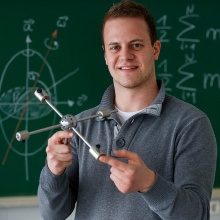 Ein Student stellt ein physikalisches Experiment vor. Im Hintergrund eine Tafel mit Formeln.. Foto: