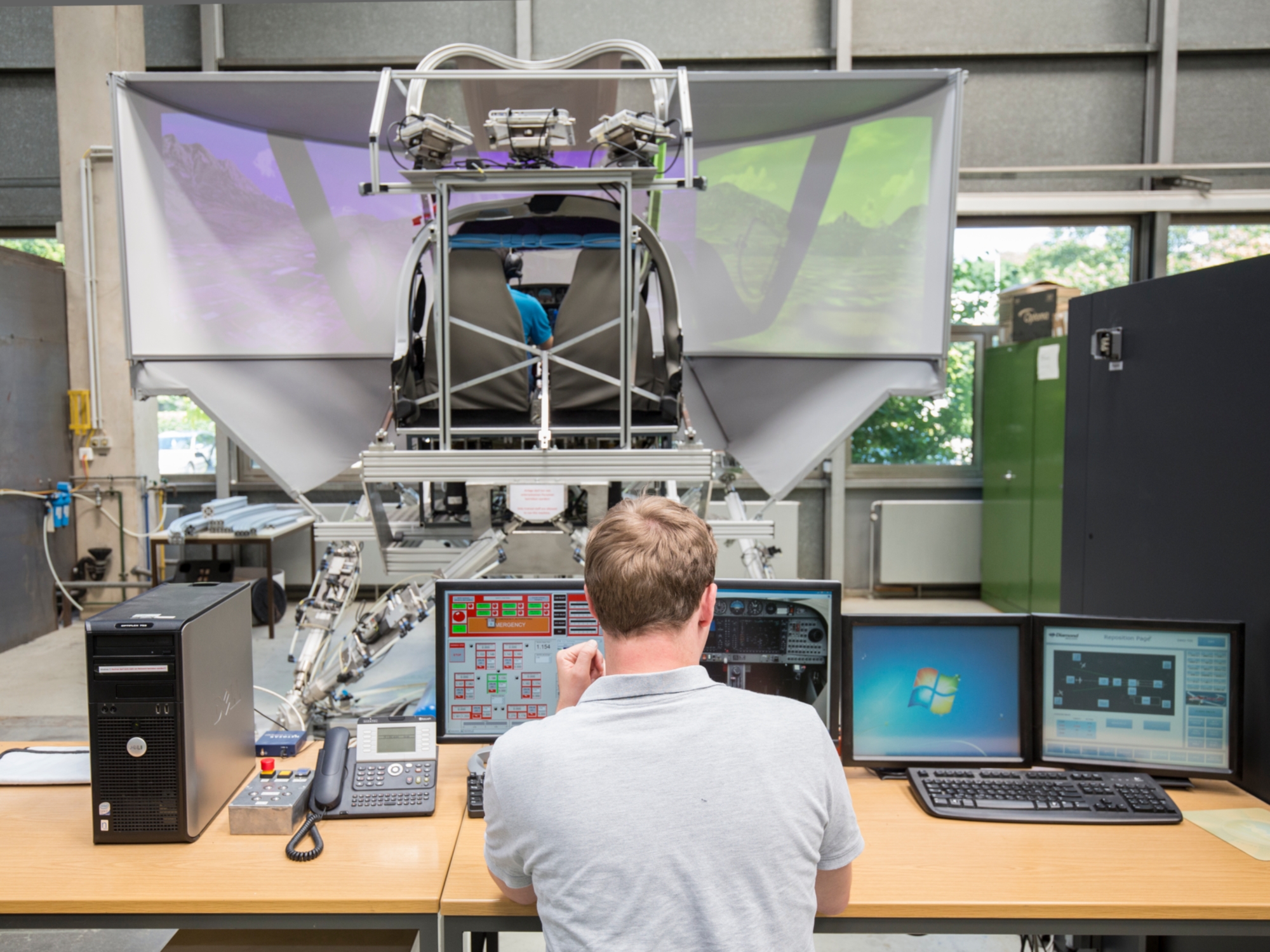 Ein Student betrachtet Computerbildschirme während im Hintergrund ein weiterer Student in einem Flugsimulator sitzt.
