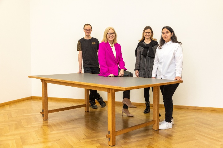 Von links nach rechts: Auszubildender Daniel Schwarz, Kanzlerin Anna Steiger, Personalentwicklerin Katrin Böhm und Auszubildende Irem Bakan, stehend am Schreibtisch der Kanzlerin.