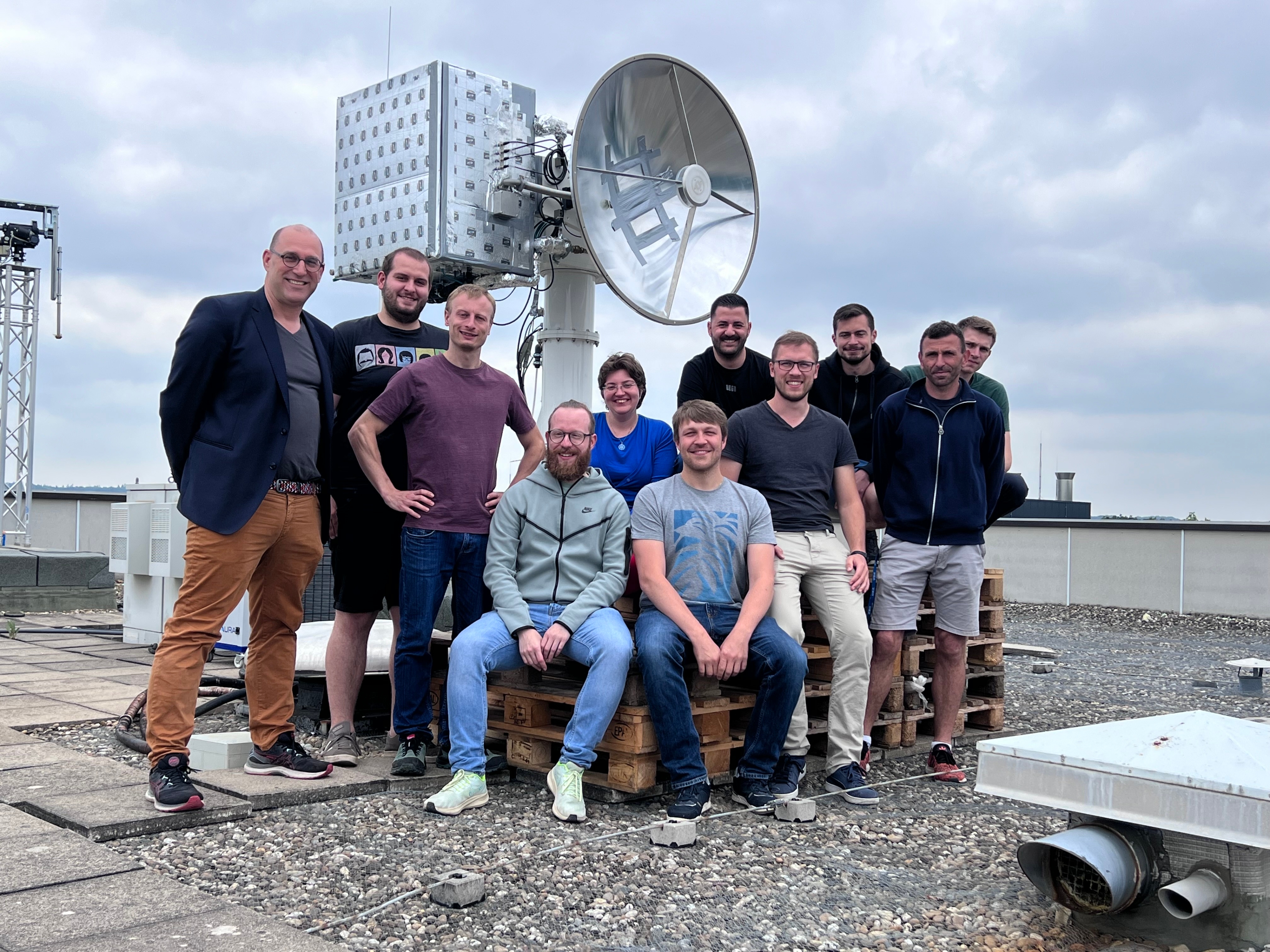 Das Forscherteam vom ILH posiert für ein Gruppenfoto vor der Bodenstation auf dem Dach des Pfaffenwalrings 31 auf dem Campus Vaihingen.