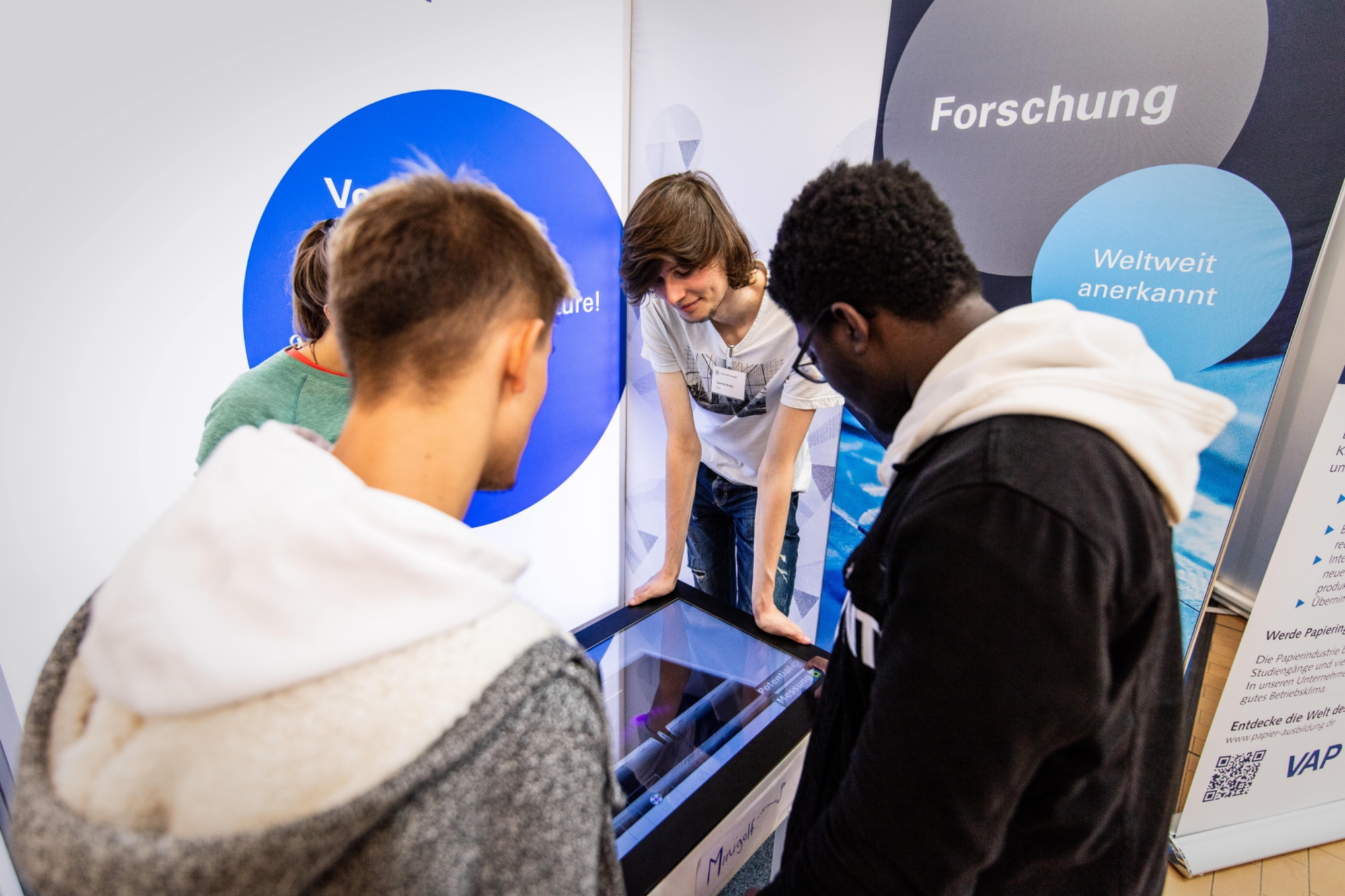 Junge Interessierte unterhalten sich am Stand der Uni Stuttgart auf der Messe.