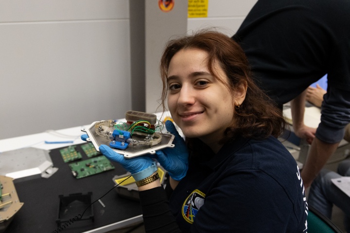 A student holds the experiment module proudly into the camera.