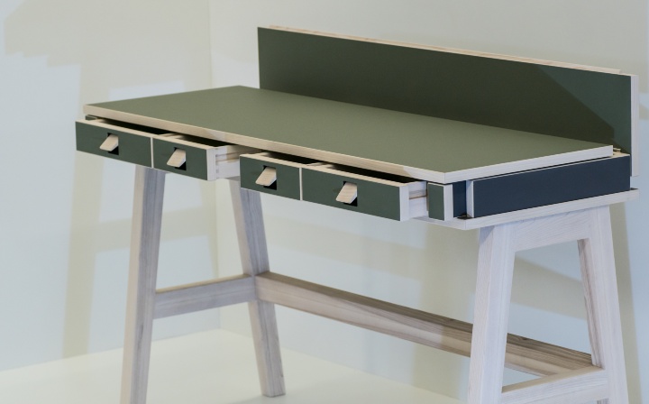 Schreibtisch aus Holz mit grüner Arbeitsplatte und blauen Schubladen.