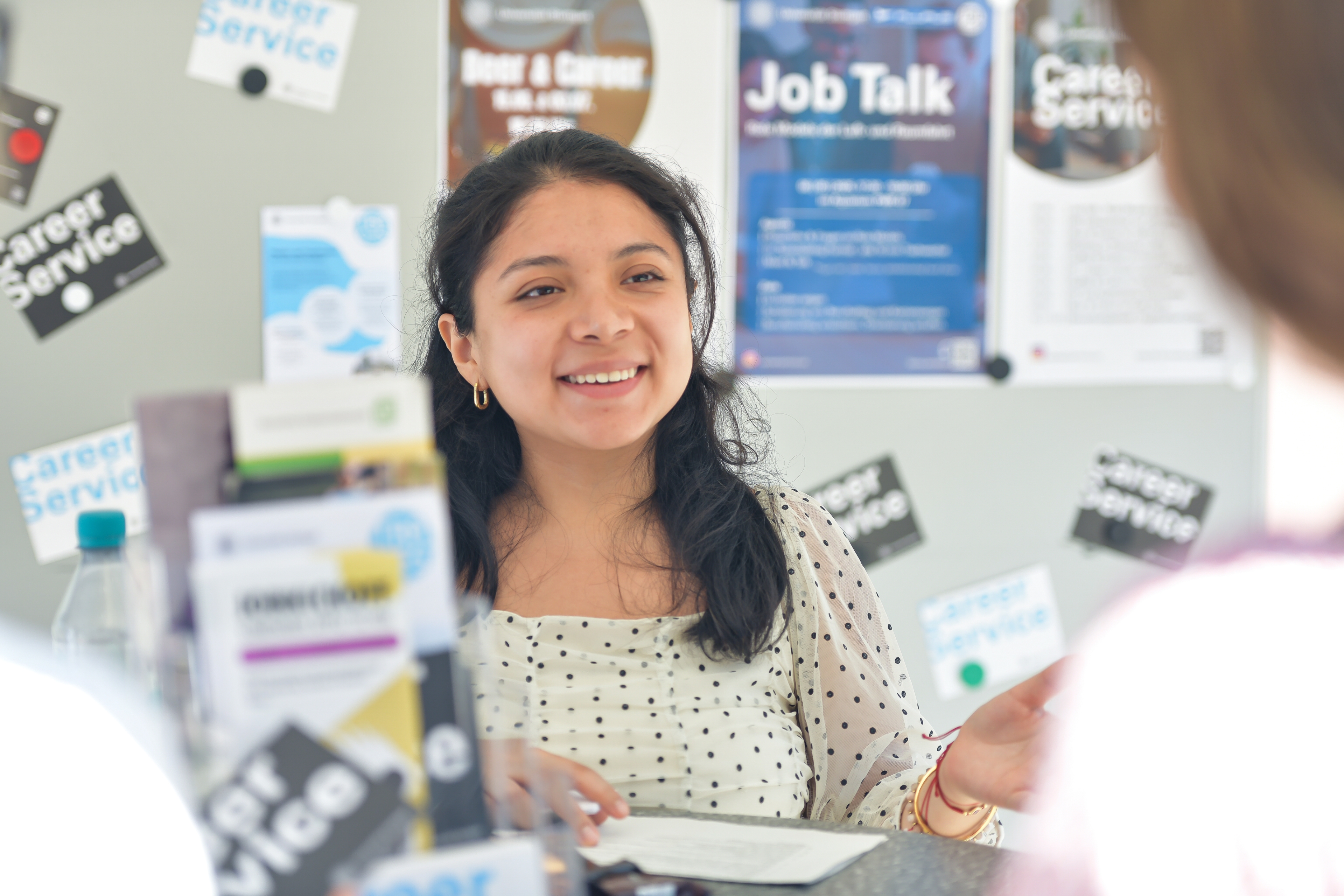 Eine junge Studentin im Gespräch mit einer Studentin an einem Stand des Career Service beim Markt der Möglichkeiten.