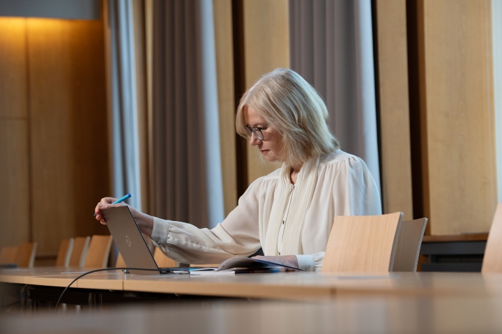 Die Kanzlerin Anna Steiger sitzt an einem Tisch im Senatssaal der Uni Stuttgart, vor sich einen aufgeklappten Laptop und ein Notizbuch.