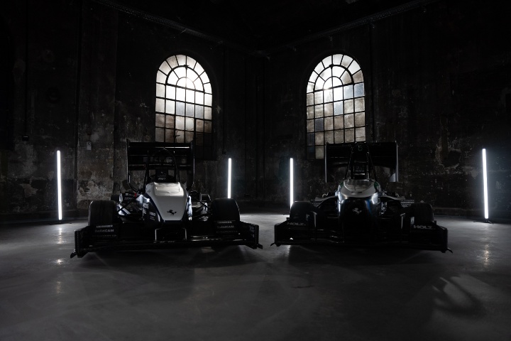 Two vehicles are parked in a darkened hall. The only light comes through two high windows in the background. The contours of the vehicles are thus only hinted at