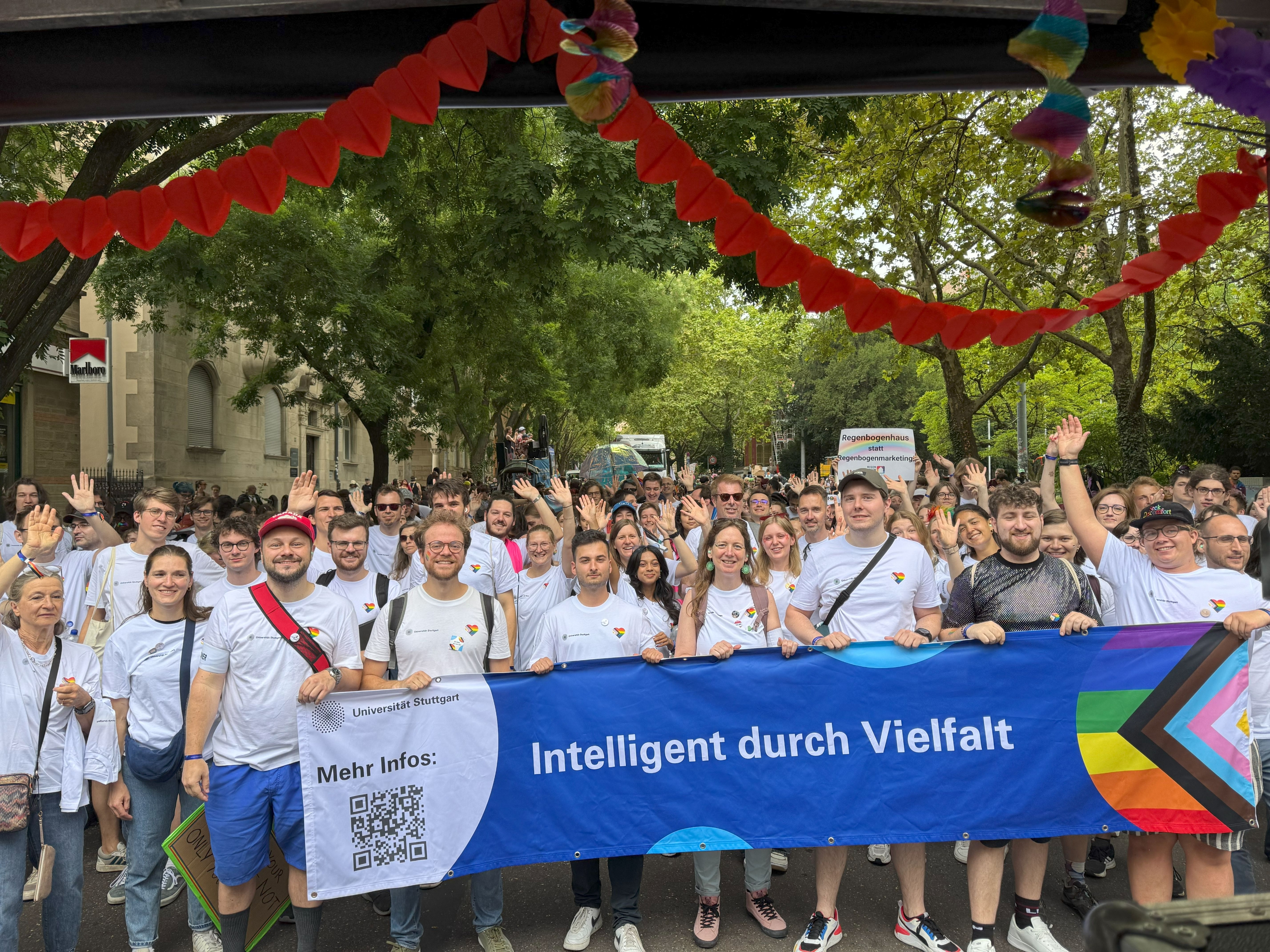Eine große Gruppe von Menschen steht hinter dem Uni-Banner, auf dem "Intelligent durch Vielfalt" steht.