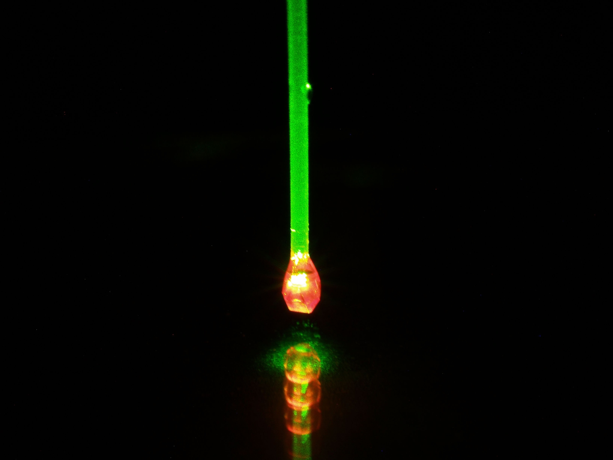 Mit grünem Laserlicht beleuchteter Diamant. Aufgrund des Fluoreszenzlichts der in ihm befindlichen Quantensensoren leuchtet er rot.