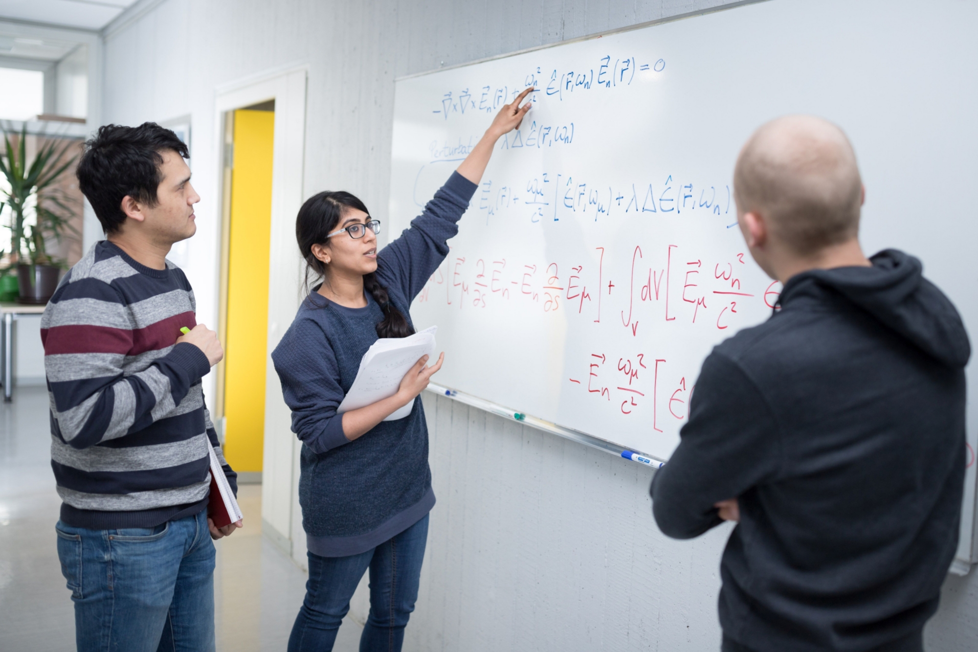 Nachwuchswissenschaftler*innen vor einer Tafel bei der Erläuterung einer mathematischen Formel.