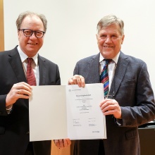 Rektor Ressel und Eberhard Grün halten gemeinsam eine Urkunde