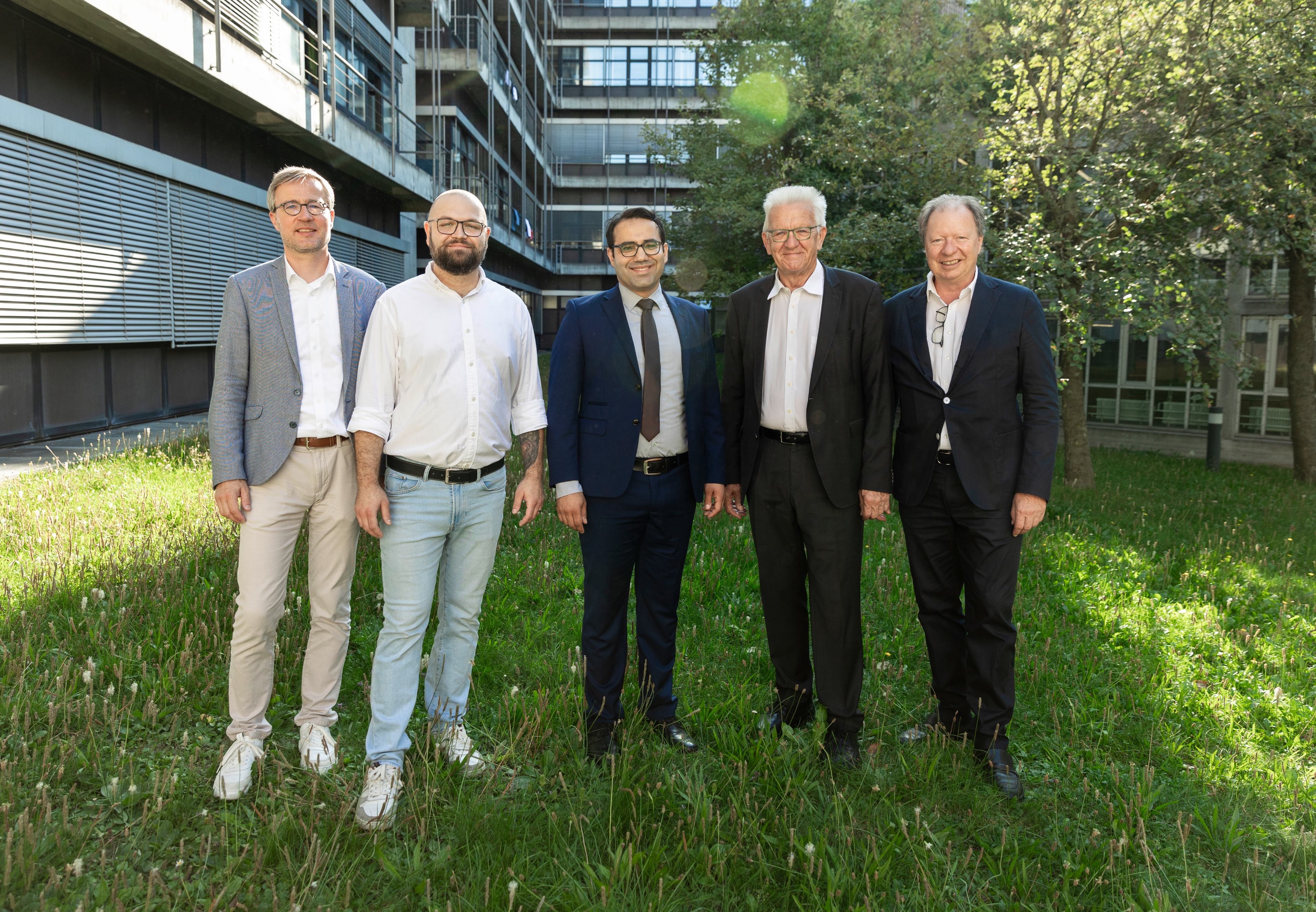 Gruppenbild im Freien, mit Gebäude und Bäumen im Hintergrund. Zu sehen sind von links nach rechts: Prof. Peter Middendorf, Prorektor für Wissens- und Technologietransfer, Dr. Claudiu Mortan, Prof. Michael Saliba, Ministerpräsident Winfried Kretschmann und Prof. Wolfram Ressel, Rektor der Universität Stuttgart.