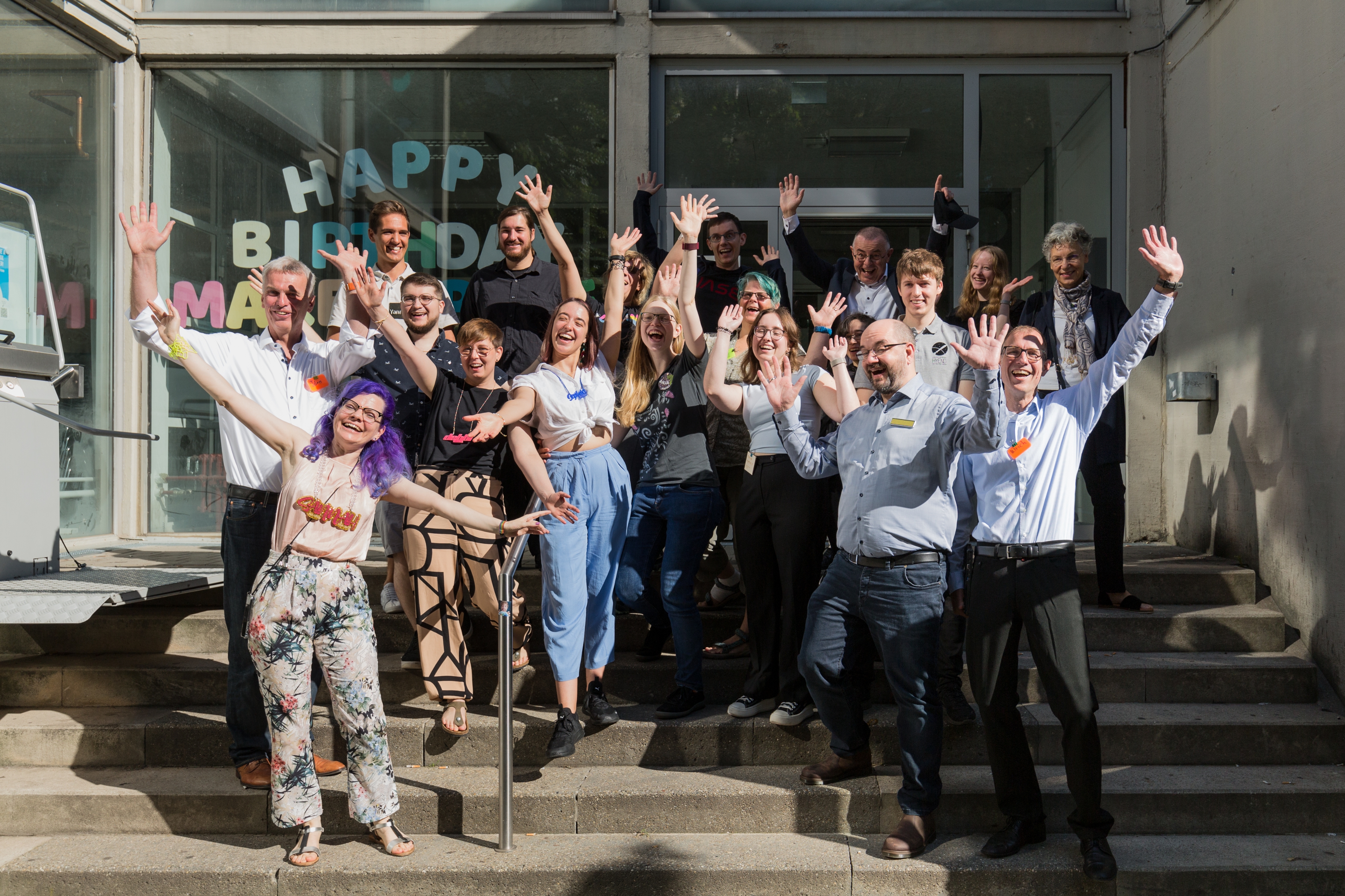 Gruppenfoto des Makerspace-Teams vor dem "Universium". Die Teammitglieder strecken die Arme in die Luft und lachen.