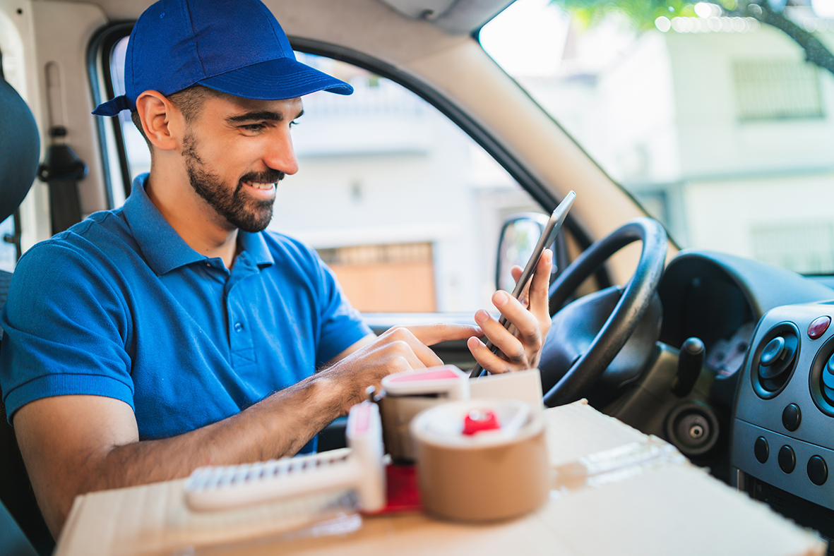 Fahrer eines Lieferwagens bei der Routenplanung pe Smartphone (Symbolbild)