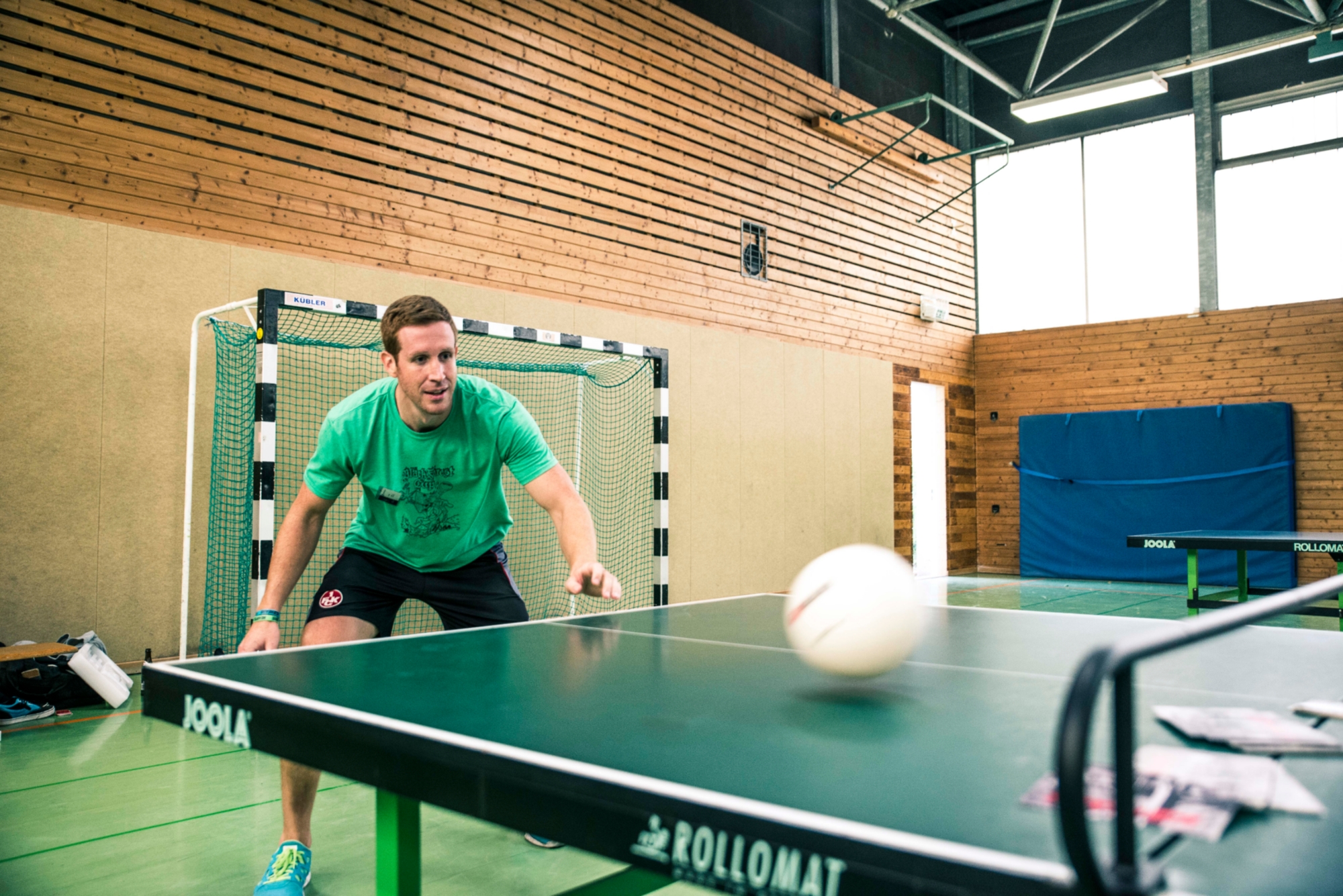 Student spielt Tischtennis in einer Sporthalle.