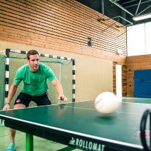 Student spielt Tischtennis in einer Sporthalle.