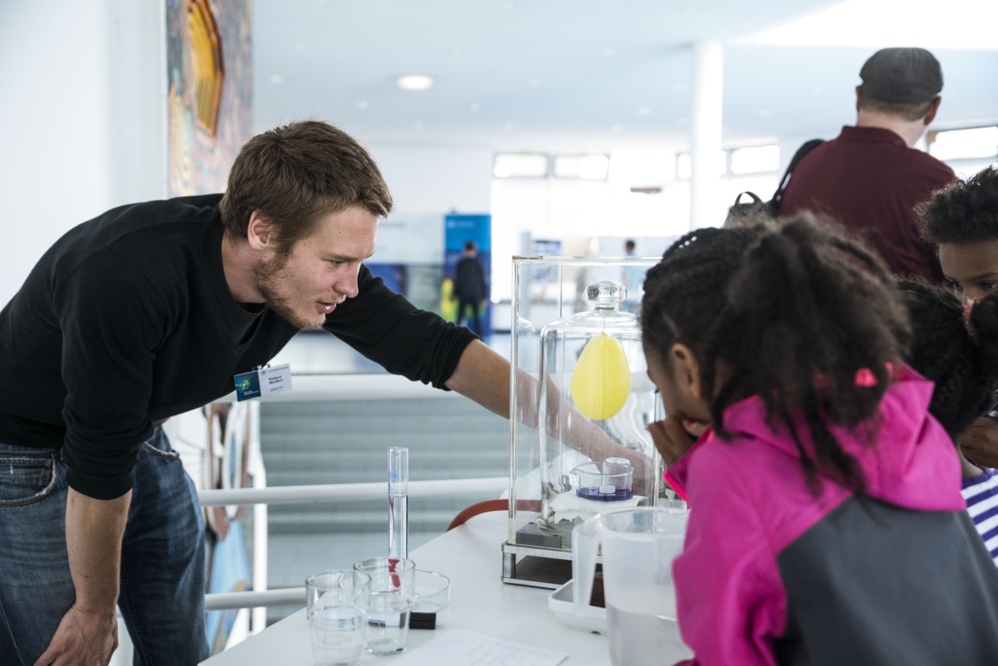 Ein junger Wissenschaftler erklärt Kindern ein Experiment mit einem Luftballon.