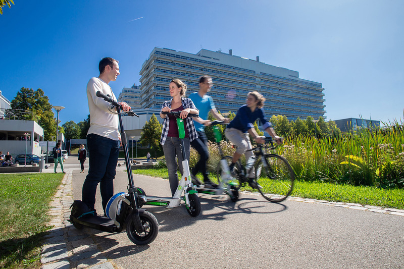 Several people with e-scooters and bicycles on the campus Vaihingen. 
