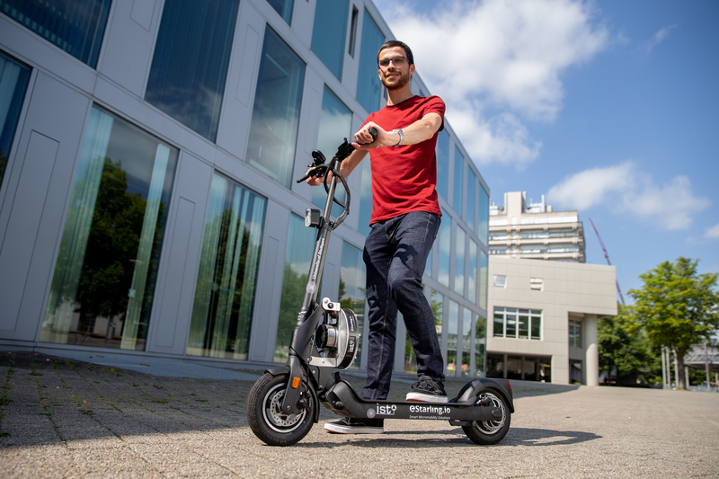 A man with an e-scooter is standing in front of a building.