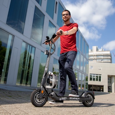 A man with an e-scooter is standing in front of a building.